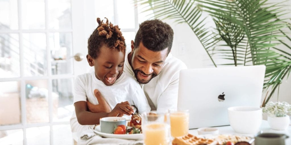 a Non-Custodial Parent looking at a computer over breakfast with his kid